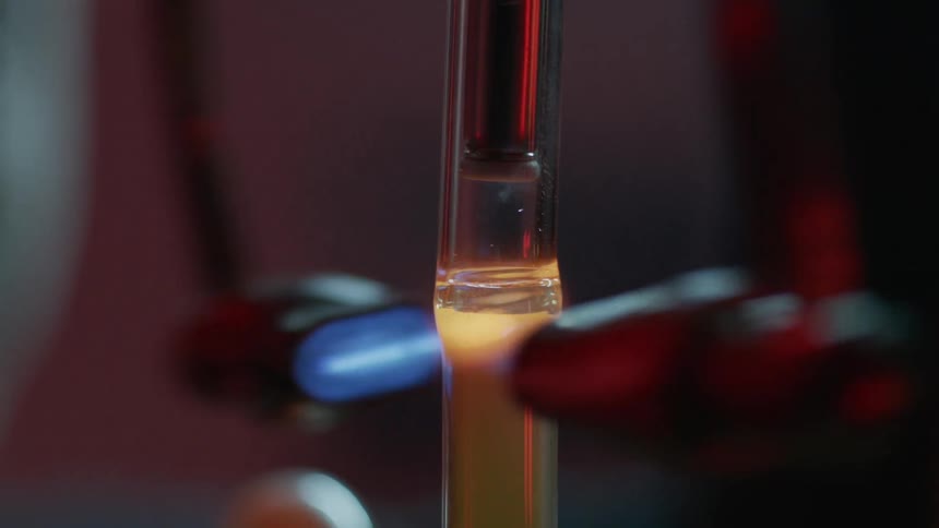 A person using a dual headed lampworking torch to heat a glass tube