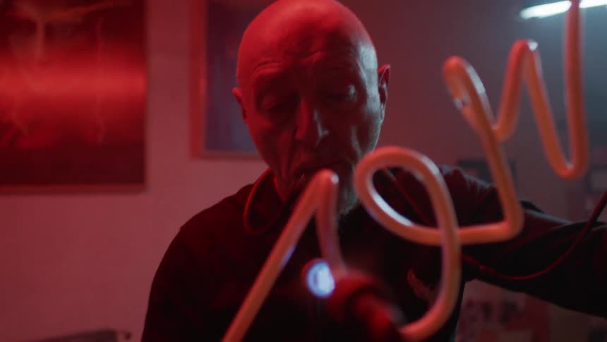 A man guides a long glass tube through a flame to shape it