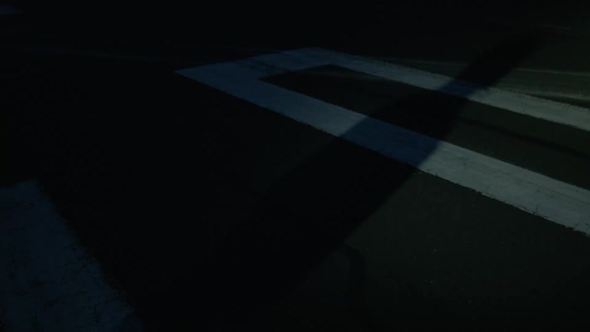 A mans shadow is shown as he stands on pavement marked with large numbers as a bright light flashes