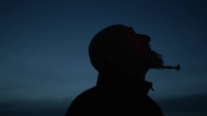 A man is covered in darkness looking up at the sky