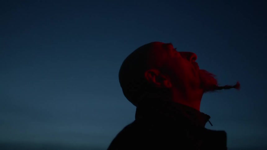 A man with a braided beard stands outside at night and looks up at the sky