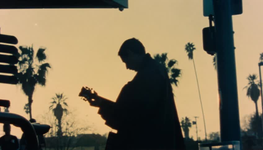 A man plays guitar on a street corner as people walk by