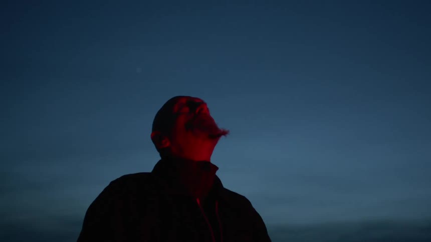 A man with a braided beard stands outside and looks up to the sky