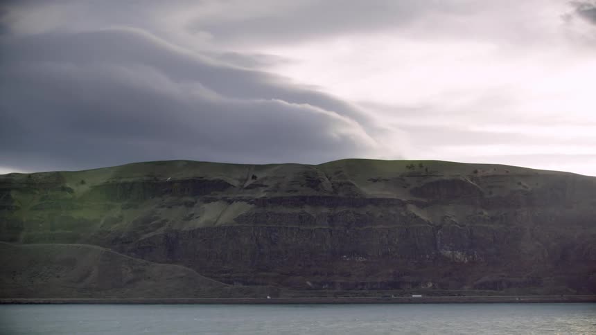 Trucks hauling goods and commerce along a rural interstate as seen from across the river with ominous clouds in the afternoon sky