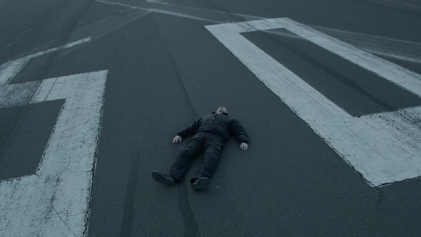 A fully clothed white man lies on pavement near painted numbers