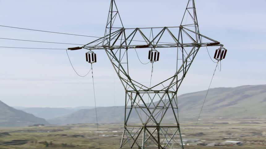 A transmission tower stands in a rural area with sweeping vistas and a mostly clear blue sky in early Spring season