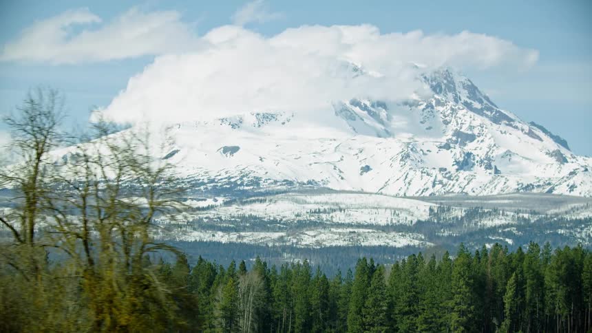 Wide shot of Mount Adams rising high above the mountain landscape on a sunny beautiful winters day as white puffy clouds cling to the mountain summmit