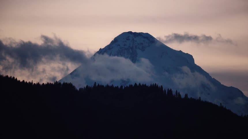Looking up after sunset at golden and purple light as low hanging clouds float in front of a snow covered Mount Hood deep in the winter months
