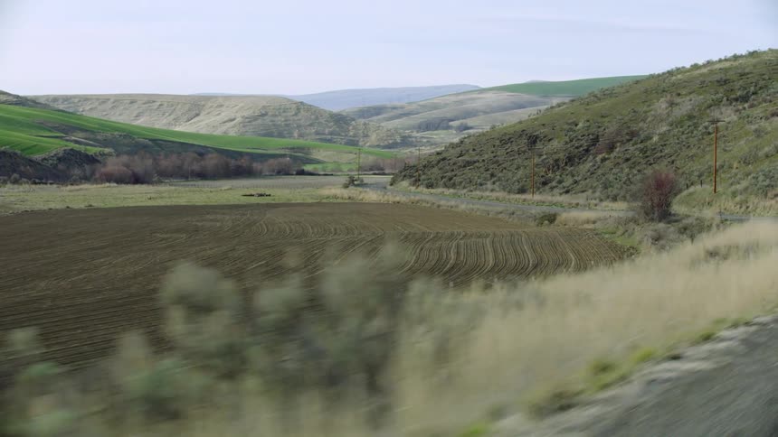 Passenger point of view looking out the window at rural agriculture in early spring as the grasses start to grow again