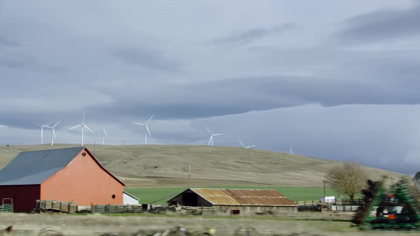 Looking out the window from the ranch truck at an old farmhouse with wind mills spinning on a distant ridge