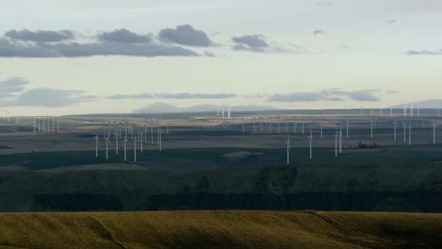 Looking across a vast canyon at hundreds of windmills far off on the horizon with white puffy clouds blowing in the sky