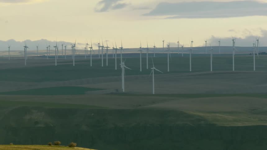 A windmill farm at sunset is seen far off on the horizon as white windmills turn in the strong wind generating tremendous amounts of clean renewable energy