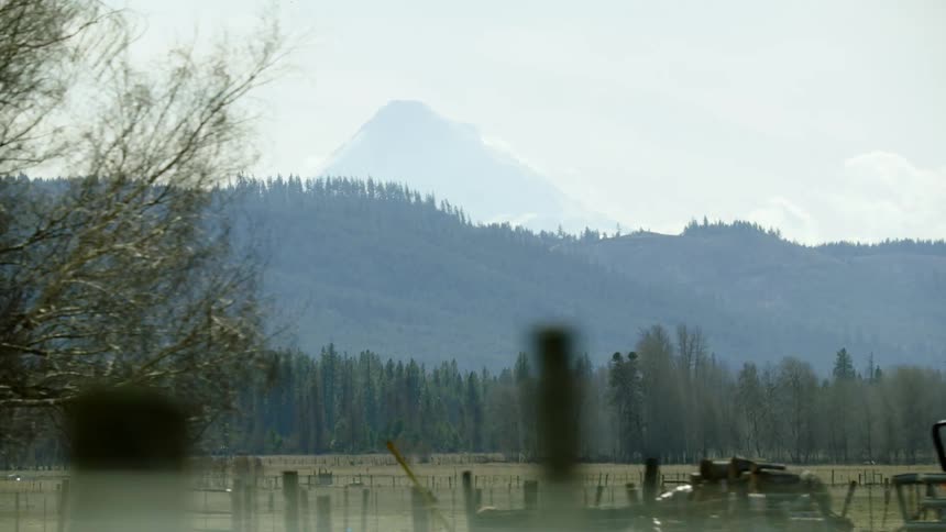Looking out the window of the passing farm truck at rural range land and a large Mount Hood in the far distance as the vehicle passes by