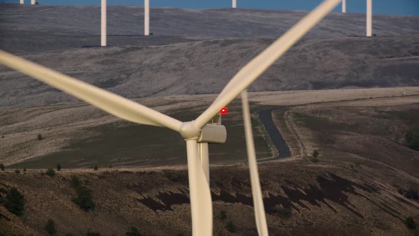 Tight shot of rotating wind mill blades at sunset with several other wind mills seen in the rural background in this dynamic shot