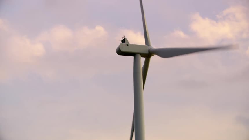 A sole wind turbine rotates on a ridge creating clean and green renewable energy in front of a beautiful sunset sky with awesome clouds