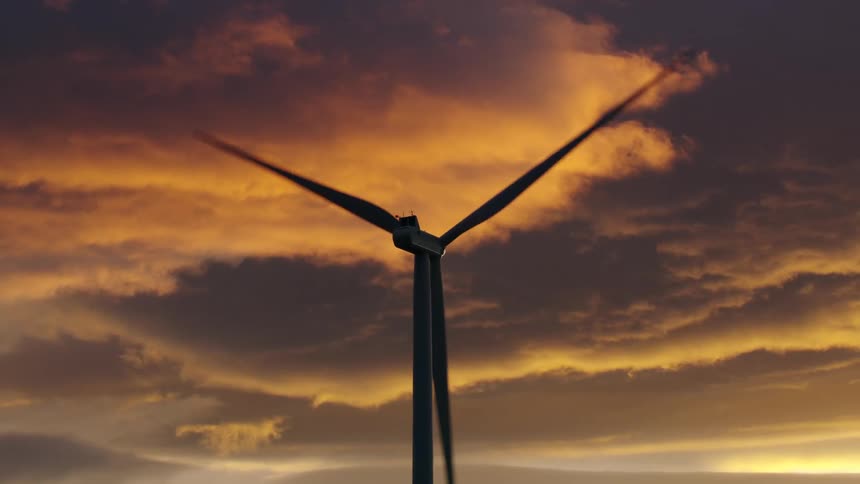Stunning sunset clouds are seen behind the silhouetted wind turbine as it creates renewable electricity for power consumption in the USA