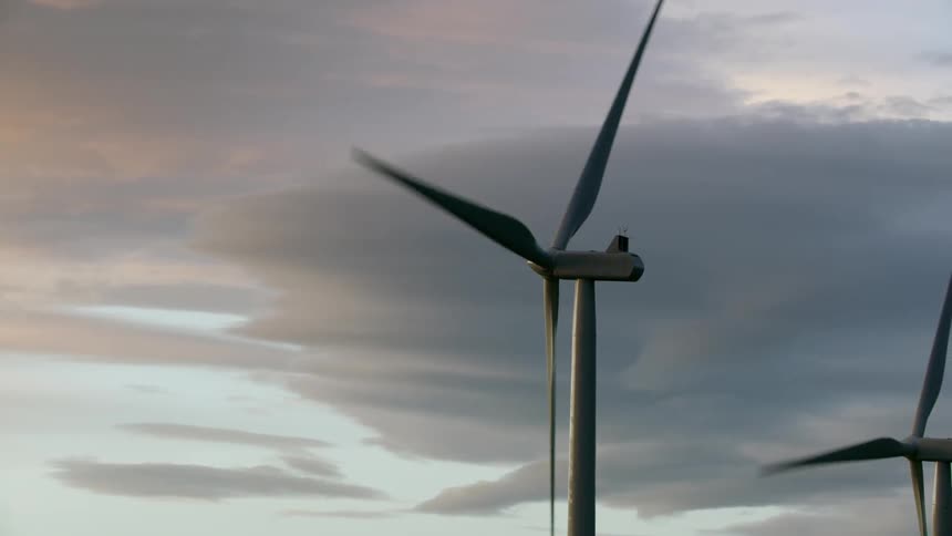Wind turbines rotate with high altitude clouds being illuminated by sunset colors creating tremendous amounts of renewable and clean green energy