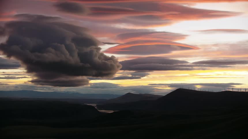 Time lapse of lenticular clouds being illuminated by the setting sun with windmills spinning in the background on the right side of the frame