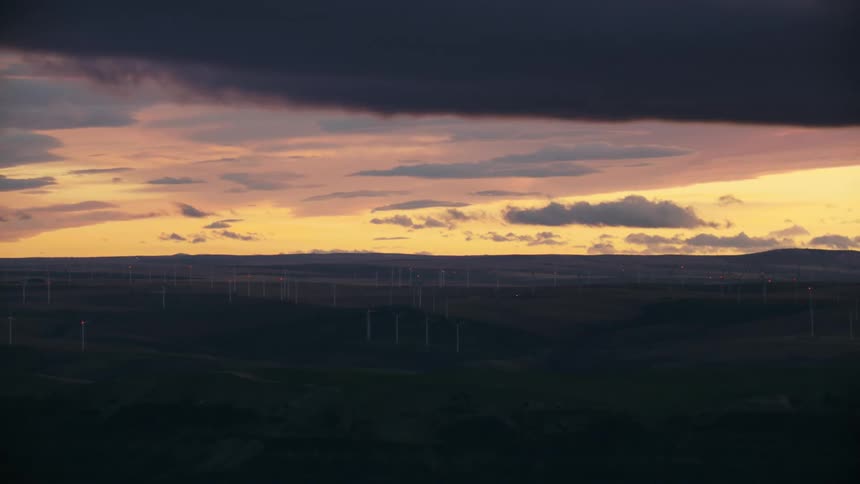 Looking across a valley after the sun has set at hundreds of windmills creating renewable power on a far away ridge