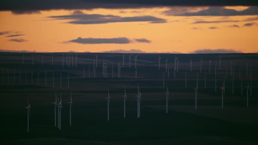 Blue hour aerial of a vast wind farm generating renewable energy in front of a golden sunset sky