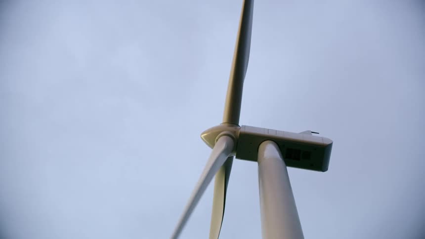 Unique shot passing directly underneath the rotating blades of a large wind mill as the camera looks up at the nacelle