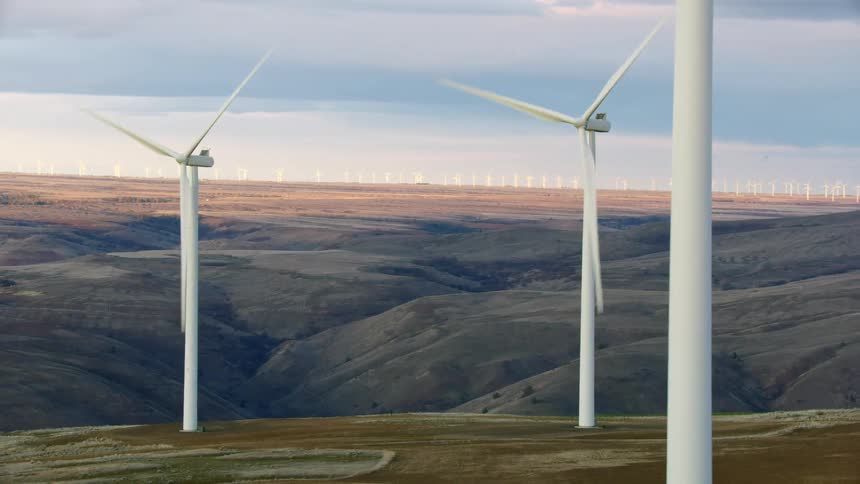 The wind mills in the foreground are turning generating renewable energy while hundreds of white windmills can be seen far of on the horizon beyond the canyon