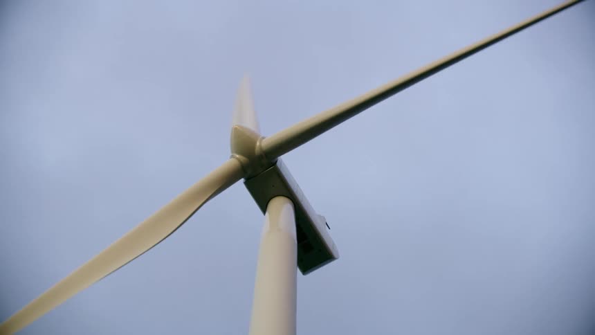 Tight shot looking straight up at the spinning blades of a wind turbine as they get radically close to the lens of the camera