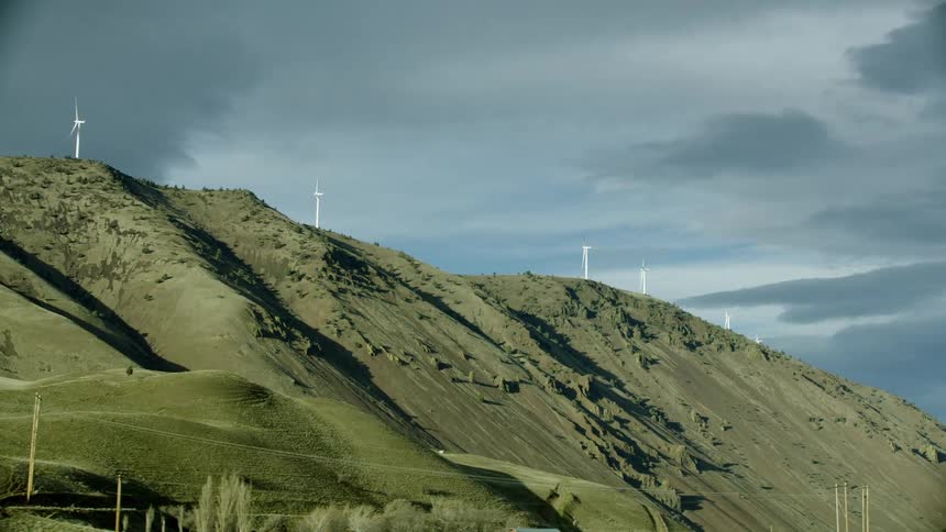 Wind turbines spin and create renewable energy high on a mountain ridge with dynamic storm clouds in the distance