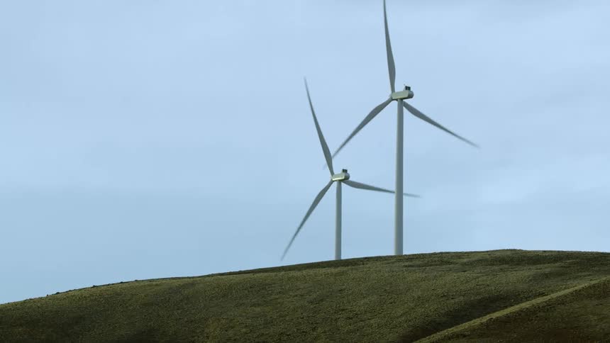 Two wind turbines rotate creating green and clean renewable energy from this low altitude lookup aerial
