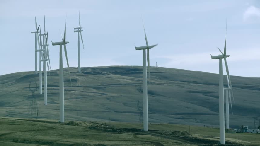 Static shot looking down a row of wind turbines as the spin on a wind farm in rural America