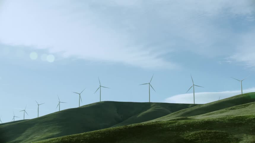 Low altitude aerial looking up at windmills high up on a mountain ridge rotating creating lots of clean and green renewable electricity