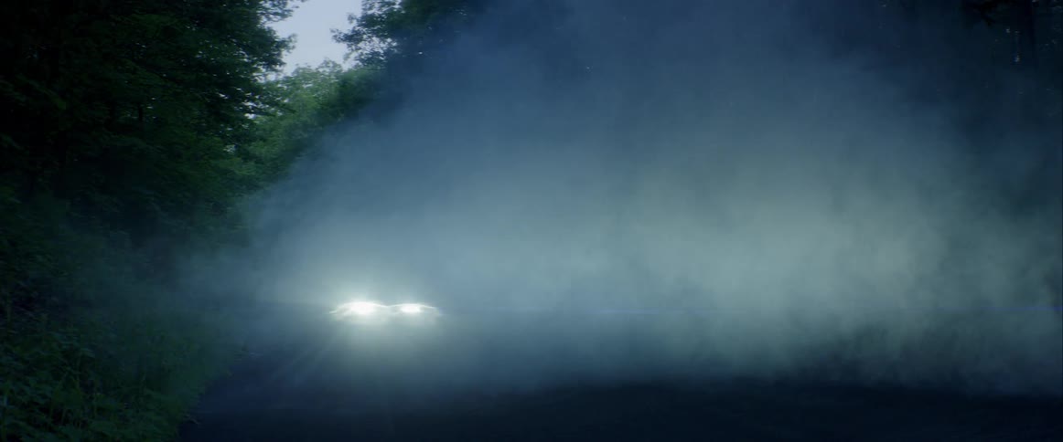 A car drives down a misty and shaded road