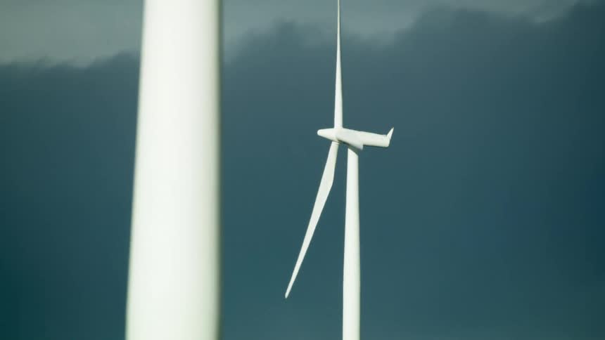 Looking up at bright white wind turbines strongly contrasted by dark storm clouds in this high energy dynamic renewable energy shot