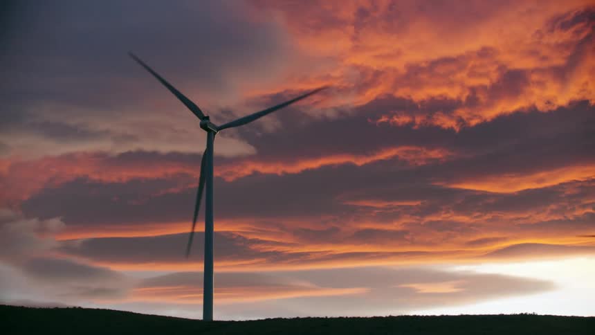 The camera orbits around a sole wind turbine with outrageous sunset clouds in the background in this beautiful and dynamic shot