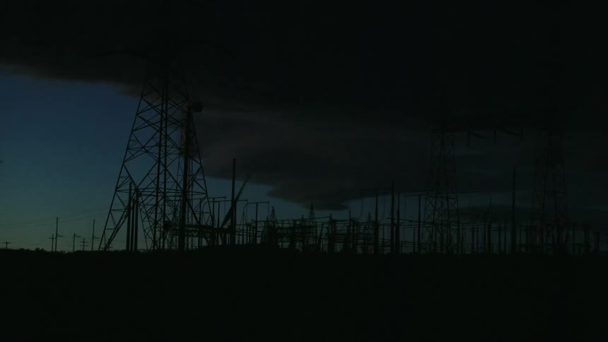 Electric transmission tower with wind turbines rotating in the background as the camera whips around to show the power sub station in this dynamic shot