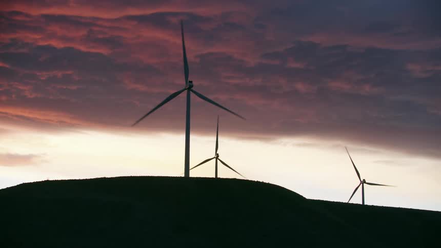 Three wind turbines whirl in the wind creating renewable clean and green energy as the sun sets and lights up the evening sky in radical colors
