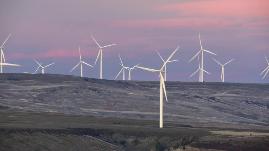 Beautiful wide angle shot of white wind turbines rotating with pink and purple clouds in the background with dry winter grasses on the hillside below