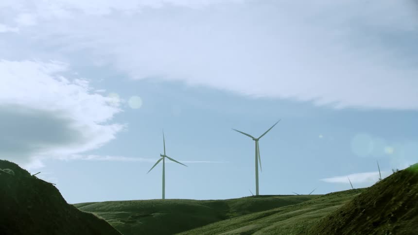 Low altitude aerial looking up at several wind mills rotating high on a ridge during spring as they generate clean and green renewable energy