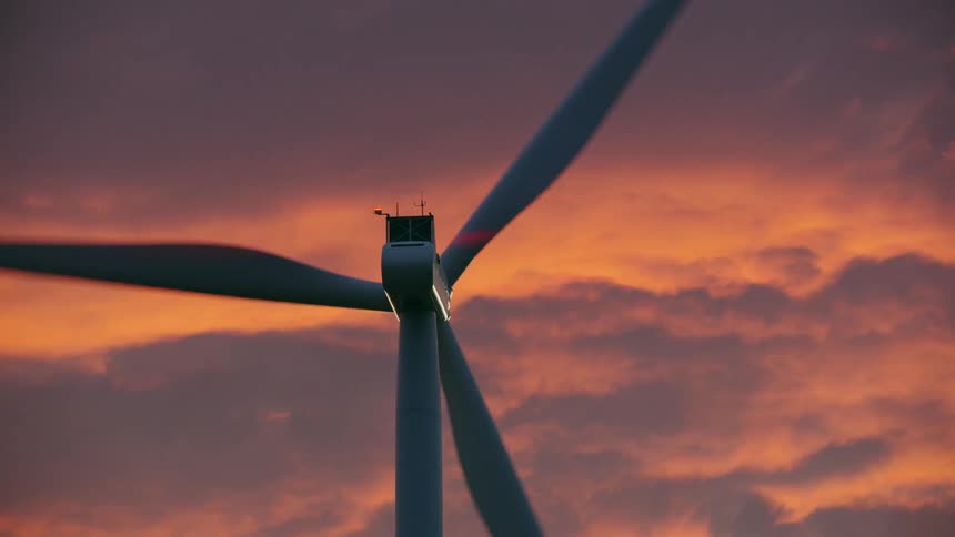 Tight shot of one windmill creating electricity in high wind with sunset pink, purple and orange clouds in the background
