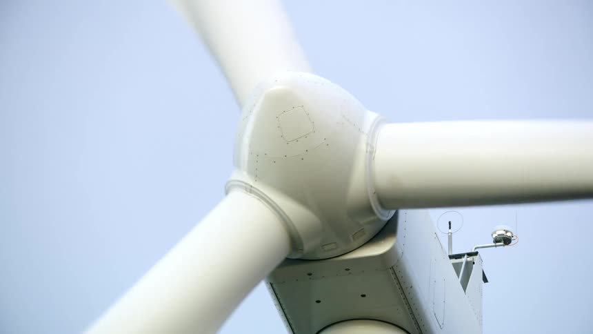 Tight shot of the nacelle of a large wind turbine as the camera zooms out revealing the dynamic foreground environment as the windmill generates renewable electricity