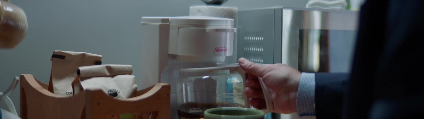An old man pours himself a cup of coffee and lifts it to smell the aroma