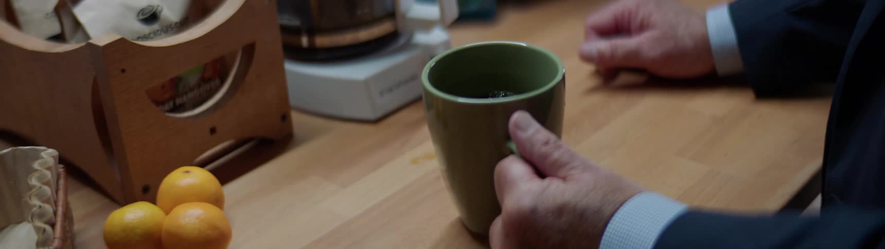 An old white male in a suit drinks coffee in a break room at an office