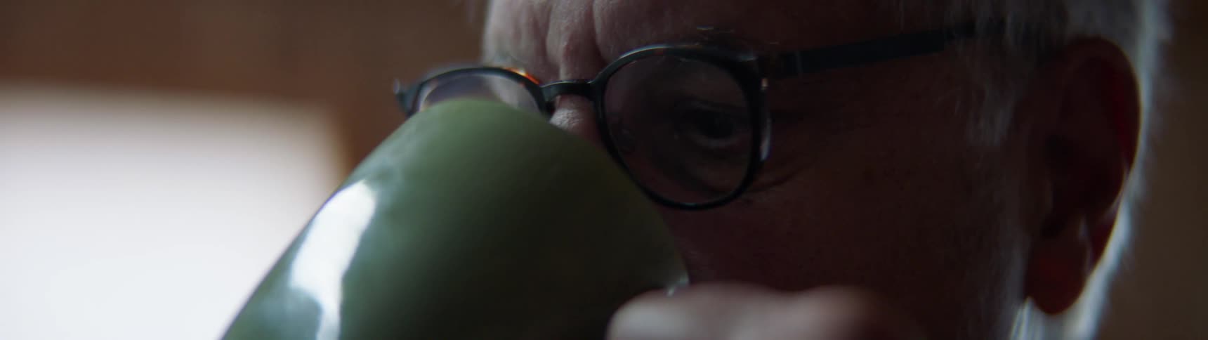 Man looks forward over green coffee mug as he drinks