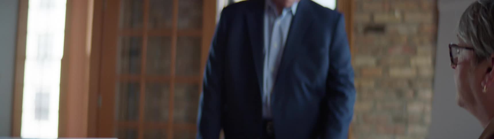 A white male in a suit speaks at an office meeting in a conference room