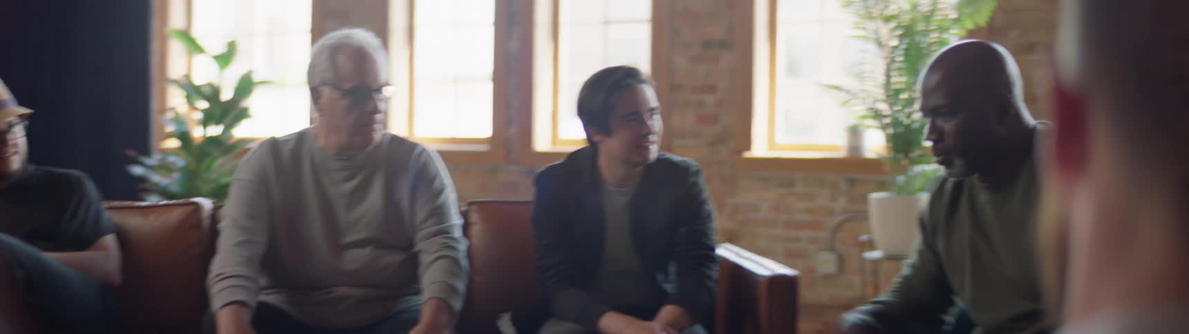 A group of men sit around in a semi circle with one man speaking to the group