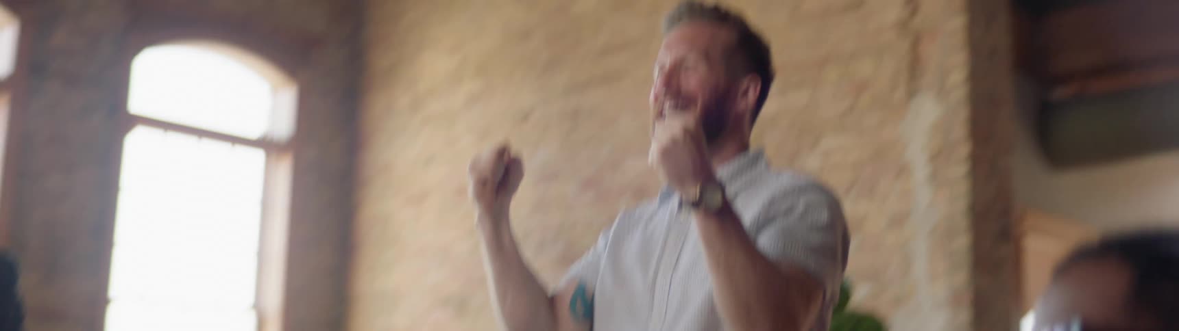 A white man stands up in a room with friends and expresses happiness and joy