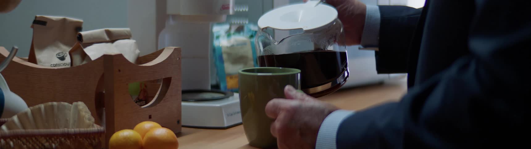 Male walks up to the counter in a break area and removes the coffee carafe from the coffee maker to pour himself a cup of coffee