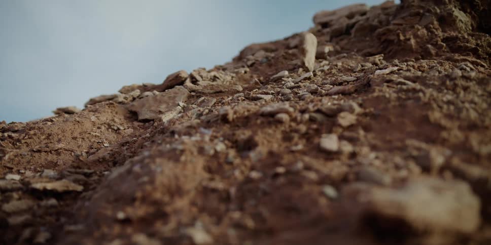 Stones and rocks roll down the side of a hill under a blue sky
