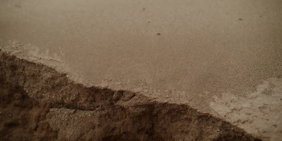 Wind blows sand over the edge of a hole in the ground