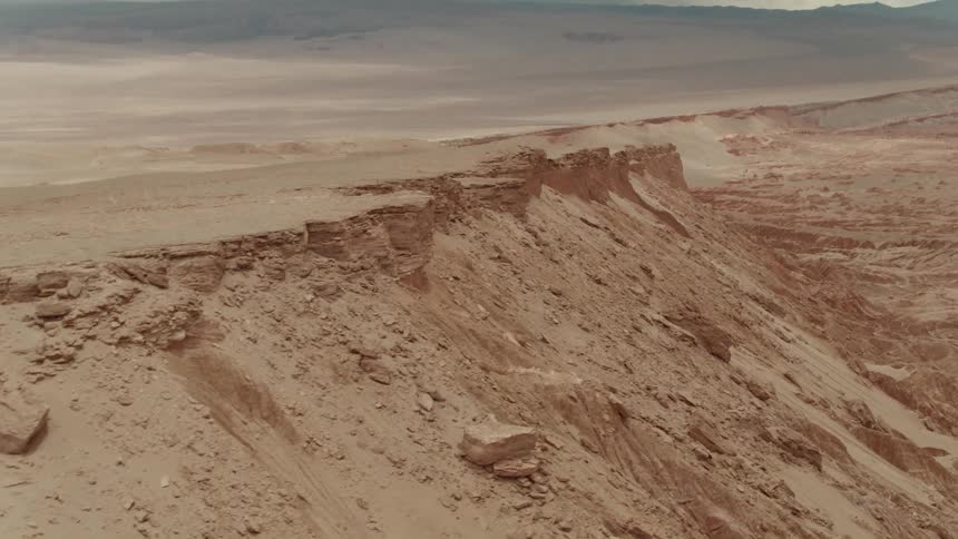A rising aerial view of a desert plateau with mountains and stormy clouds in the distance